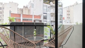 A balcony with wicker chairs and a small table, overlooking a cityscape with buildings and greenery. - MOT Rentals + Zapiola 2300 'D' - Loft Belgrano (Belgrano)