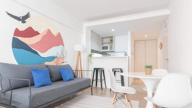 A modern living room with a gray sofa, white chairs, a dining table, and a kitchen in the background. - MOT Rentals + Zapiola 2300 'D' - Loft Belgrano (Belgrano)