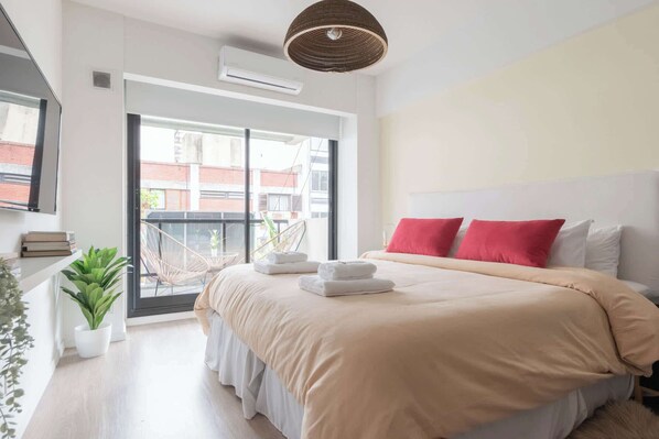 Un dormitorio moderno con una cama grande, un balcón y vistas a edificios.