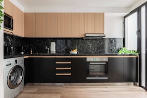 A modern kitchen with wooden cabinets, a black countertop, a built-in washing machine, and a dishwasher.