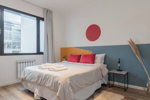 Ein modernes Hotelzimmer mit einem großen Bett, einem Heizkörper, einem Fenster mit Vorhängen, einer Wandlampe und einer Zimmerpflanze.