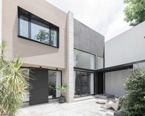 A modern house with a flat roof, large windows, and a courtyard with plants and seating.