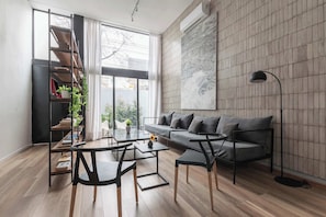 Ein modernes Wohnzimmer mit Sofa, Couchtisch, Stühlen, einem Bücherregal und einem großen Fenster mit Vorhängen.