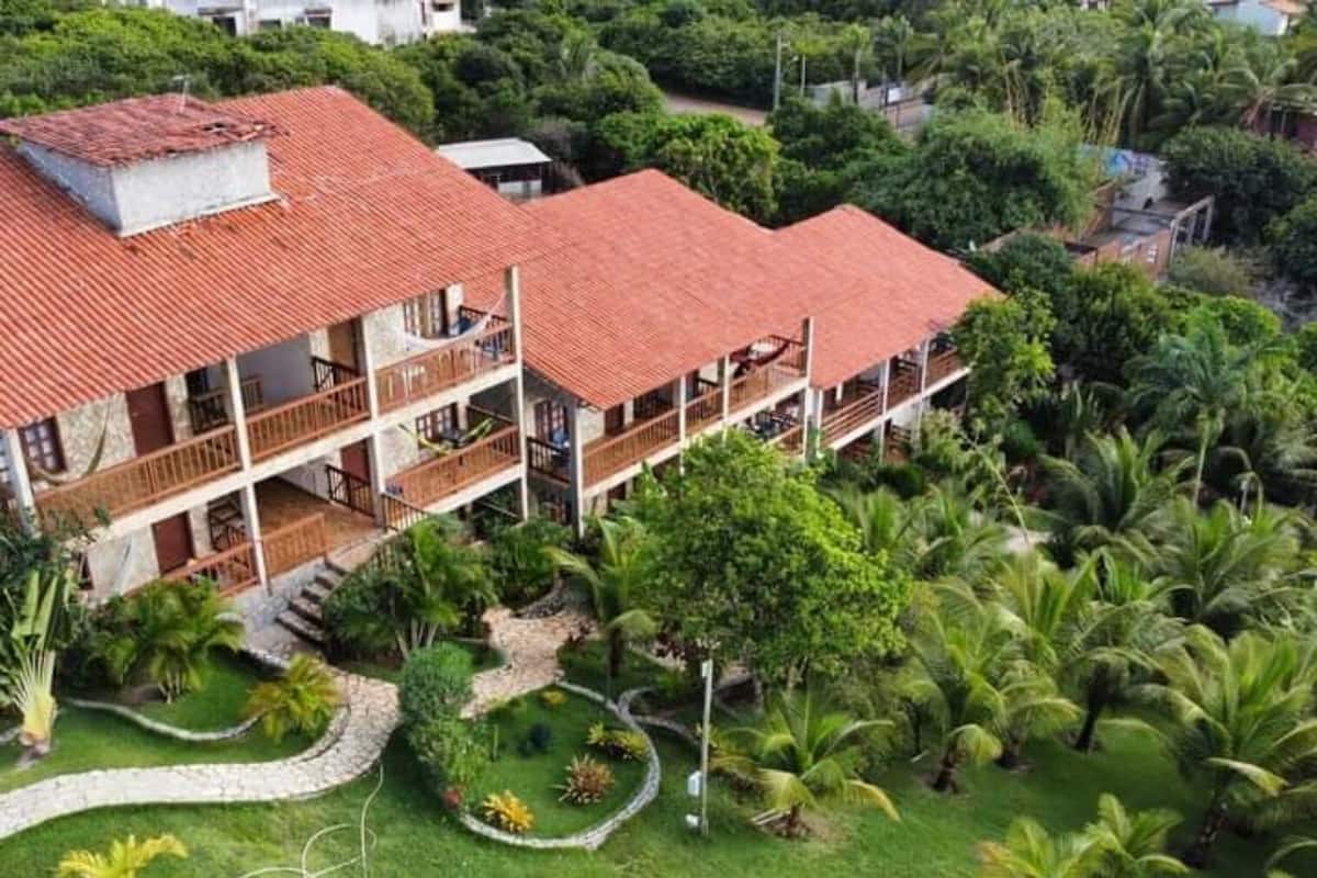 Um edifício de vários andares com telhado de telhas vermelhas, cercado por vegetação exuberante e palmeiras.