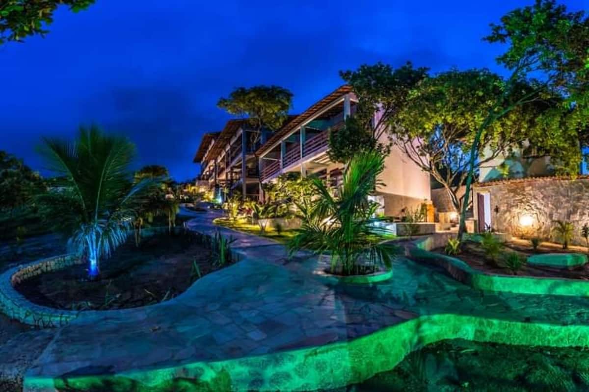 Resort com área de piscina, palmeiras e um edifício com vários andares.