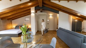 Amplio dormitorio tipo loft con techo alto, vigas de madera, cama, sofá y una mesa de comedor de vidrio.