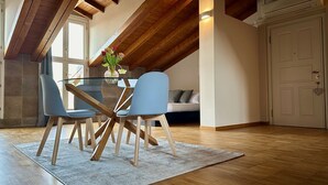 Un comedor con una mesa de vidrio, dos sillas, un jarrón con flores y techo de madera.