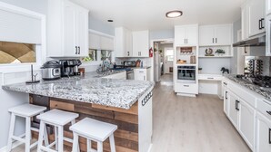 A modern kitchen with white cabinets, granite countertops, and a central island with bar stools. - The Ultimate Family Getaway- Game Room/Pool/Hot Tub/Human Chess! (Escondido)