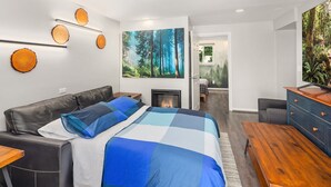 Quarto moderno com uma cama grande, lareira, escrivaninha e vista para uma floresta pela janela.