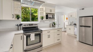 Uma cozinha moderna com armários brancos, uma geladeira de aço inoxidável, forno embutido e micro-ondas.
