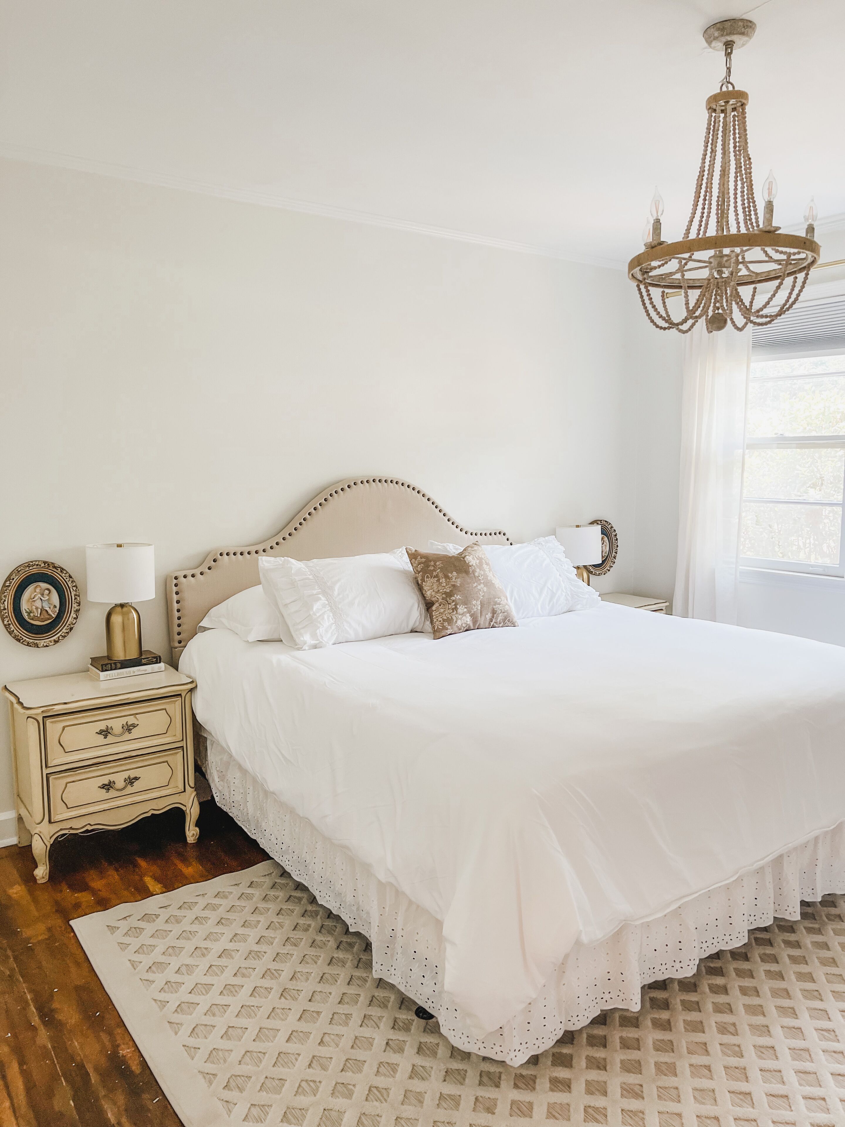 A bedroom with a large bed, a nightstand with a lamp, and a chandelier.