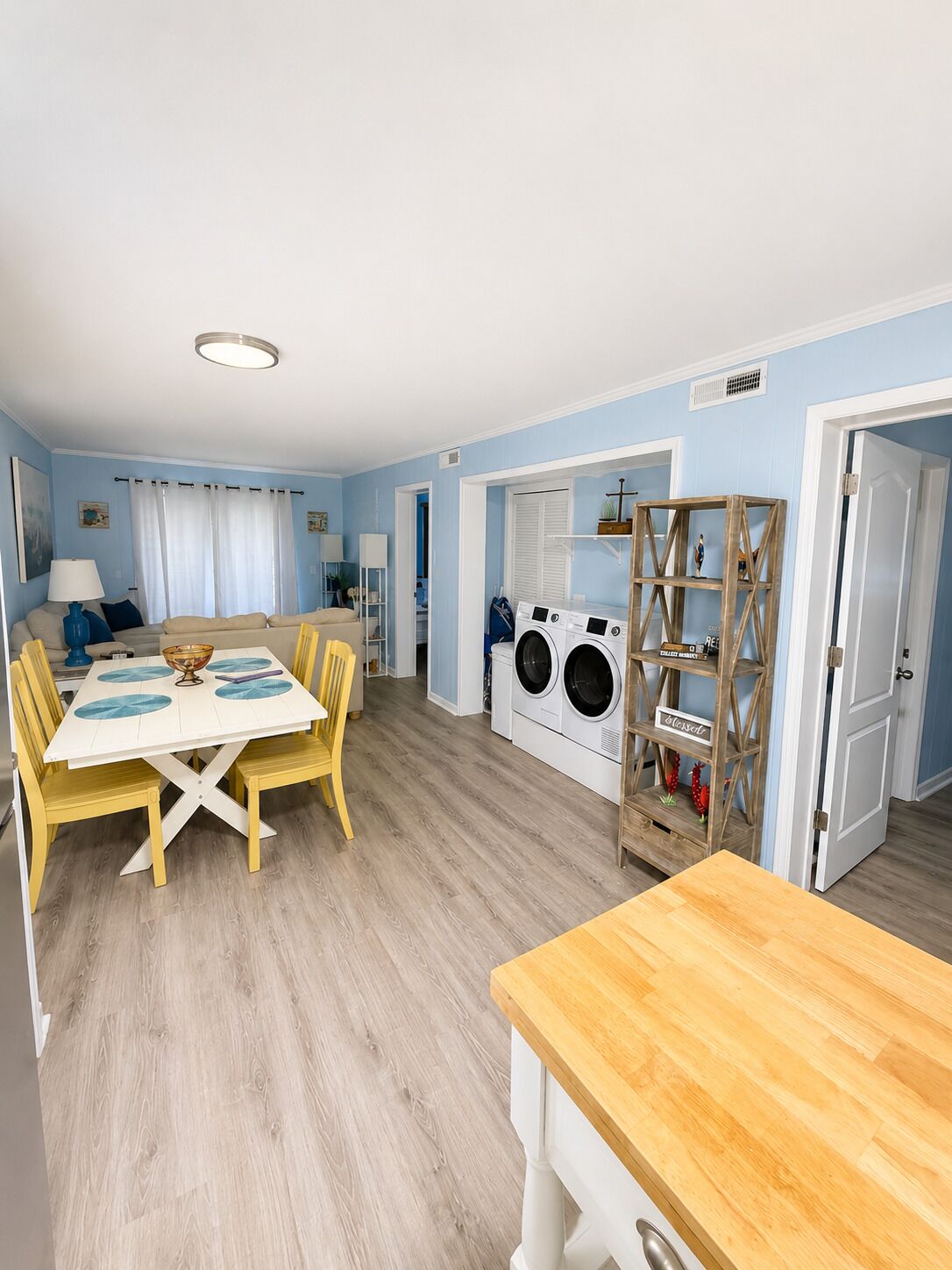 A room with a dining table, chairs, a washing machine, and a shelf with decorative items.