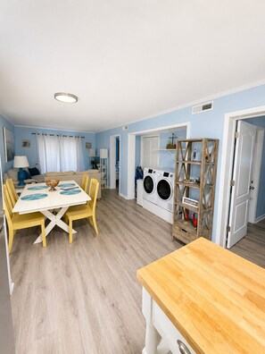 Une pièce comprenant une table à manger, des chaises, un lave-linge et une étagère avec des objets décoratifs.