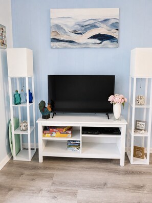Un salón con una televisión de pantalla plana sobre un mueble blanco, rodeado de estantes con diversos objetos.