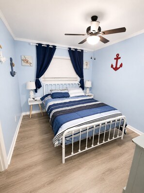 Une chambre à coucher avec un lit, des tables de chevet, un ventilateur de plafond et une décoration sur le thème de la marine.
