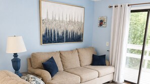 Una sala de estar con un sofá color beige, una lámpara azul y un cuadro abstracto grande en la pared.