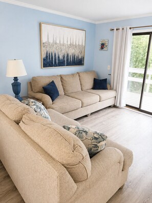 A living room with a beige sofa set, a blue lamp, and a large abstract painting on the wall. - Hilton Head Island Beach & Pickleball Getaway (Hilton Head Island)