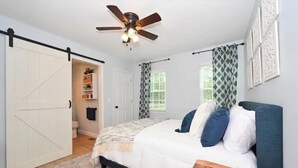 A bedroom with a bed, a ceiling fan, a wardrobe, a window with patterned curtains, and a door leading to a bathroom. - Relax at The Blue Bird - 2BD/2BA + Easy Parking (Good Hope)