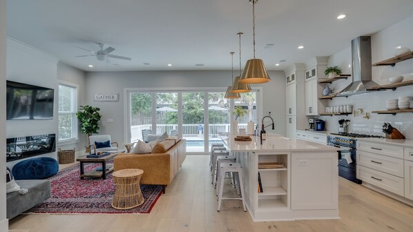A modern kitchen with white cabinetry, a central island, and a dining area with a sofa and chairs. - Beachside Bliss •Private Pool • Bikes • Walk to Beach • Pets • Sleeps 8 (Santa Rosa Beach)