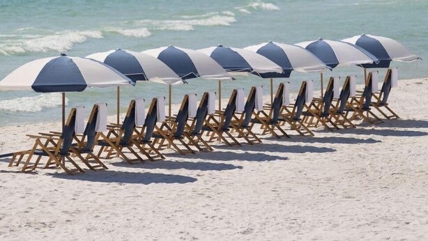 Ein Strand mit Liegestühlen und Sonnenschirmen, ein klarer Himmel und das Meer im Hintergrund.