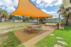 An outdoor patio area with a table and chairs, a sofa, and a large shade sail.