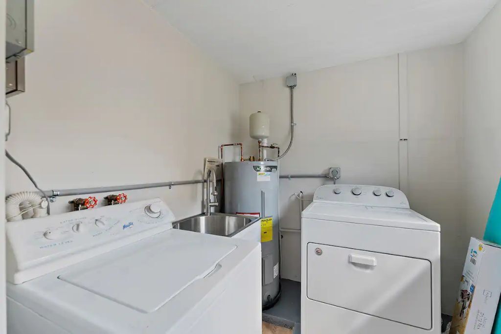 Un cuarto de lavandería con lavadora de carga frontal, secadora de carga superior y calentador de agua.