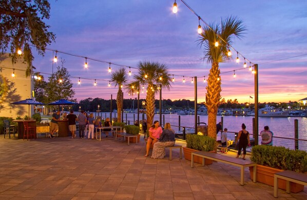 Een terras buiten met lichtslingers, palmbomen en uitzicht op de jachthaven.