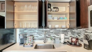 A modern kitchen with a built-in dishwasher, a coffee station, and a variety of glassware and dishes on open shelves. - Pet Friendly in Orlando area near Disney (Celebration)