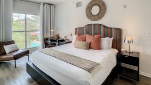 A hotel room with a large bed, a desk, a chair, a nightstand, and a view of the outdoors. - Pet Friendly in Orlando area near Disney (Celebration)