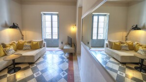 A room with a checkered floor, two sofas with yellow and patterned cushions, a small table, and a mirror reflecting the room. - Charming & traditional apartment in Valletta ESCH2 (Valletta)