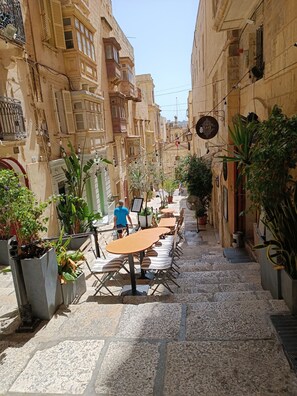Un carrer estret amb terrasses a l'exterior, plantes en testos i arquitectura tradicional.
