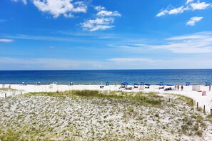 A beach with white sand, blue umbrellas, and a clear blue sky. - Beachfront condo with heated pool - walk to The Hangout (Gulf Shores)