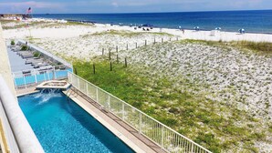Une piscine située à côté d’une plage, avec une clôture et des parasols.