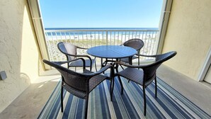 Un balcon avec une table ronde et quatre chaises en osier, donnant sur une plage.