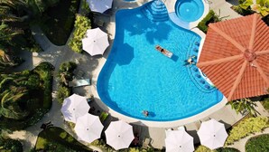 Ein großer, ungewöhnlich geformter Pool mit mehreren Bereichen, umgeben von weißen Sonnenschirmen und Liegestühlen.