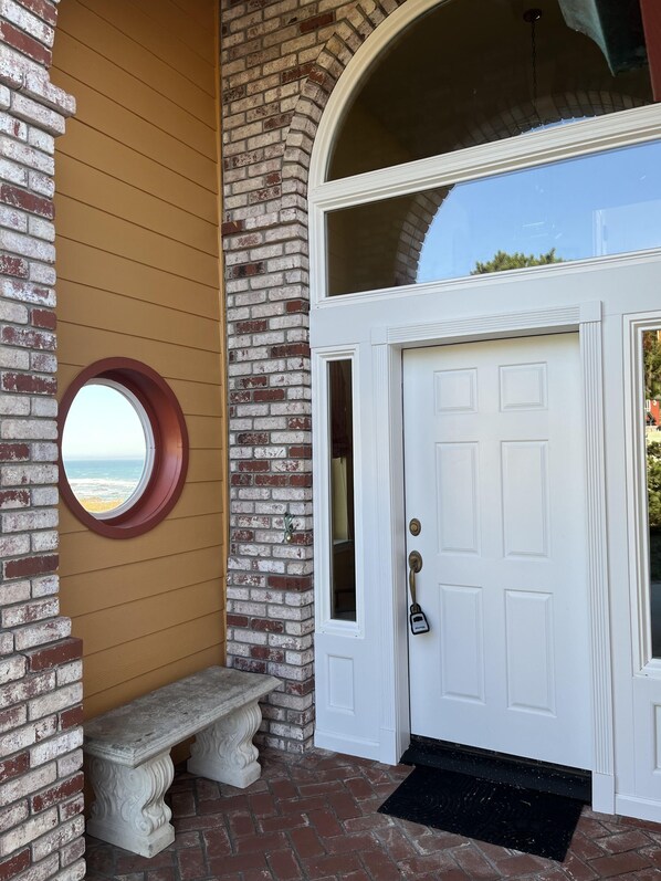 A white door with a glass panel, a stone bench, and a circular window overlooking the ocean.