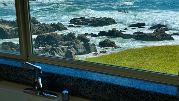 Une vue sur l’océan, aperçue à travers une fenêtre, avec un plan de travail en granit et un robinet.