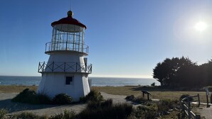 Un phare avec un sommet rouge, un corps blanc et une enceinte en verre, situé sur une zone herbeuse d’où l’on peut admirer la mer.
