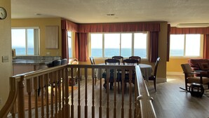 Un espace repas offrant une vue sur l’océan, doté d’un plancher en bois et d’un escalier menant à un niveau supérieur.