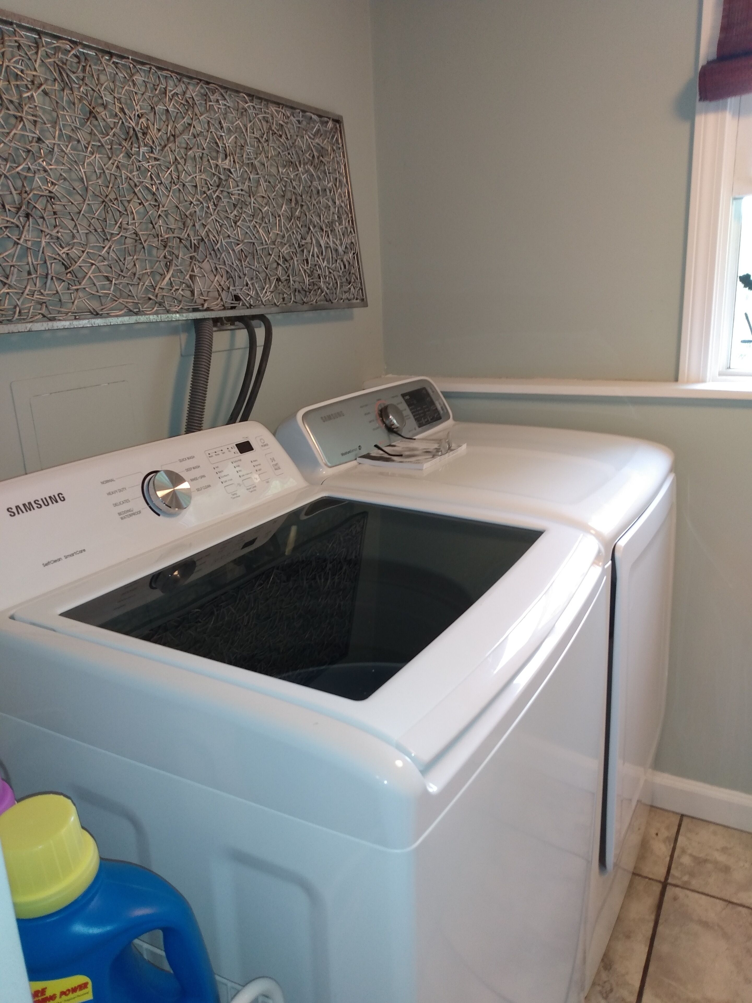 A Samsung front-loading washer and dryer in a laundry room with a patterned wall and a window.