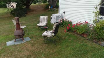A backyard with a grill, two covered chairs, and a small table.