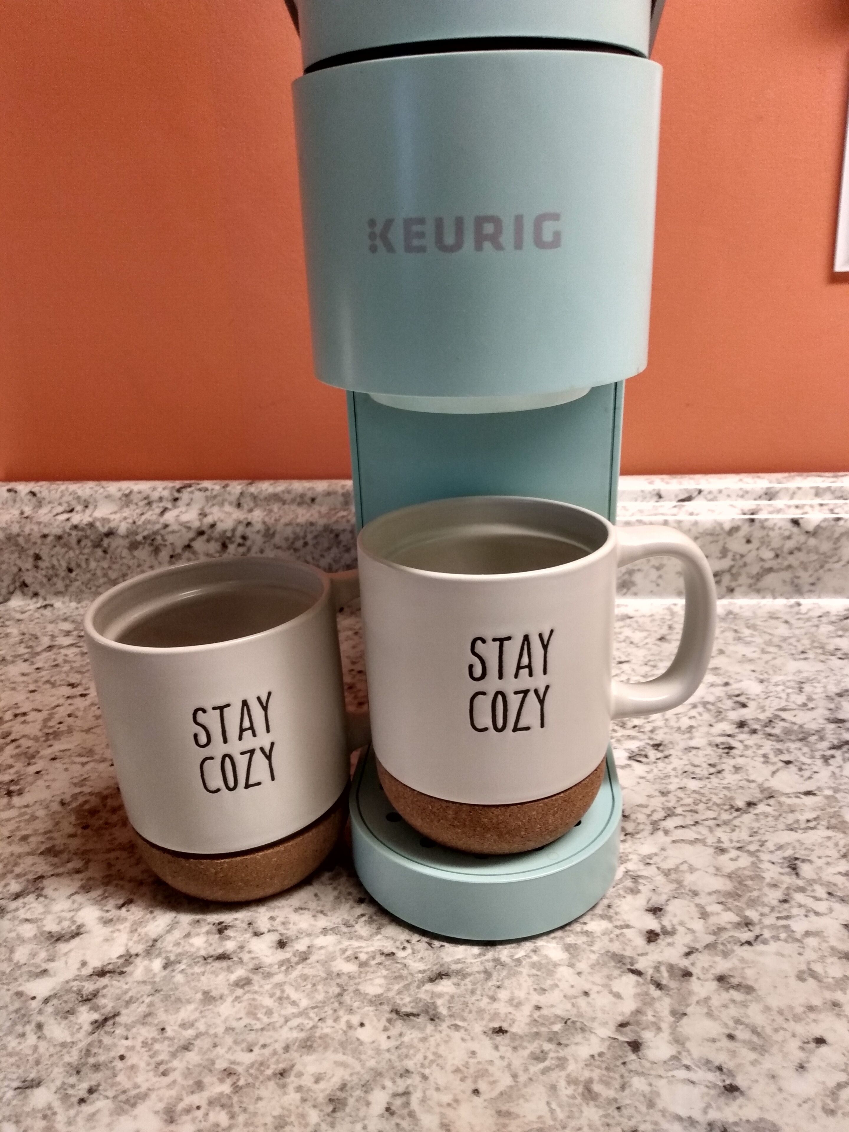 Une machine à café Keurig avec deux tasses sur son socle, chacune portant l’inscription « RESTEZ AU CHAUD ».