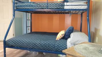 Een stapelbed met een blauw metalen frame en gewatteerde beddengoed, een houten nachtkastje en een kamerkleed met patroon.