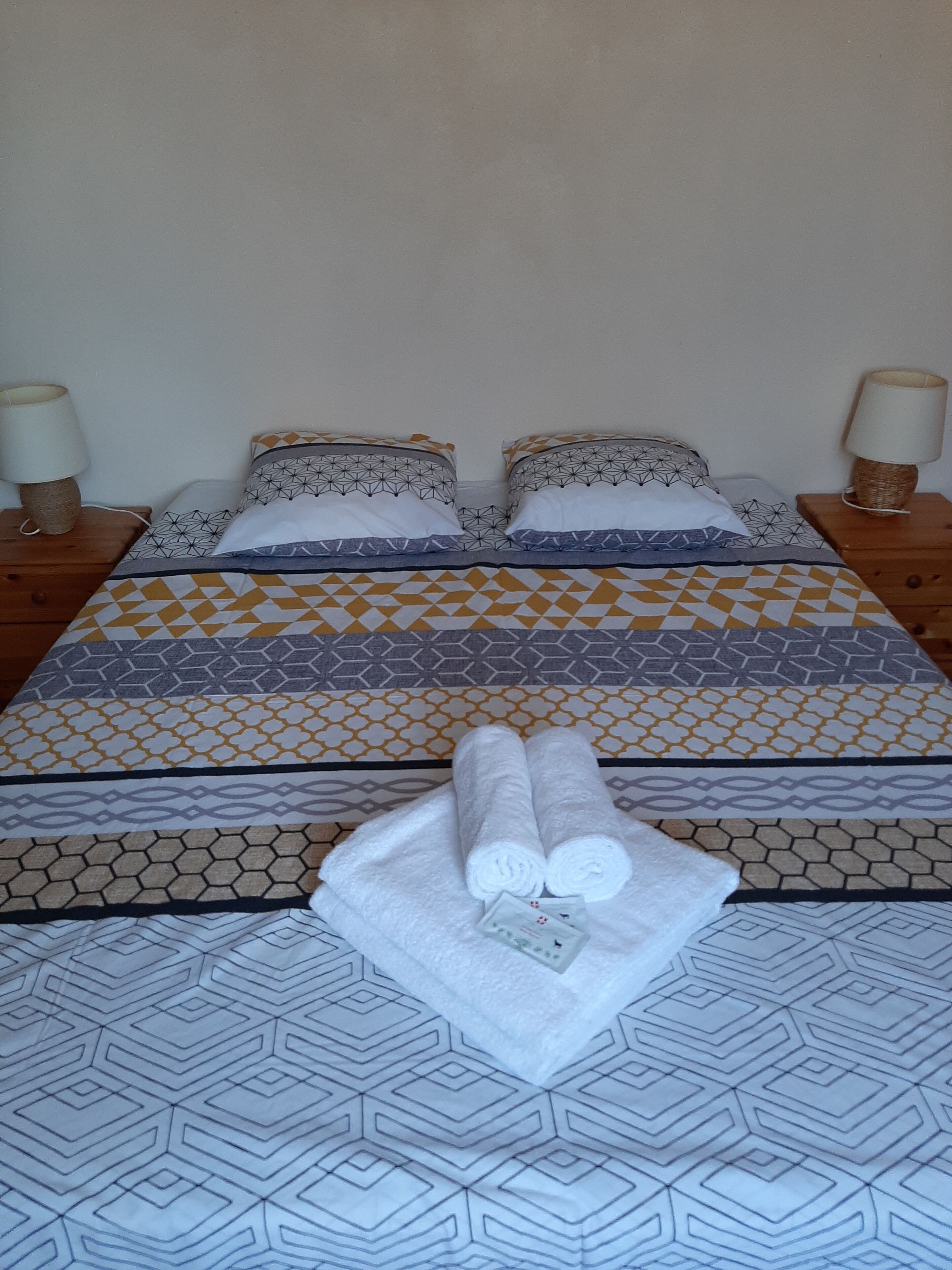 Una cama bien hecha con ropa de cama estampada, dos lámparas de noche y una toalla doblada sobre la cama.