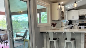 A modern kitchen with white cabinets, a large island with bar stools, and a sliding glass door leading to a patio area. - Serenity awaits at this secluded riverfront property (Muscoda)