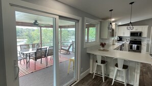A modern kitchen with white cabinets, a central island with bar stools, and a sliding glass door leading to an outdoor patio area. - Serenity awaits at this secluded riverfront property (Muscoda)