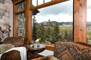 Enjoy a panoramic view of the surrounding mountains from the large window in this cozy room, featuring a patterned sofa and a small table.
