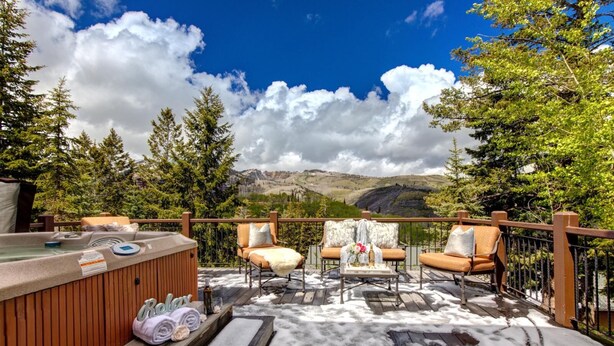 Una terraza al aire libre con un jacuzzi, dos sillones acolchados y una mesa con un florero.