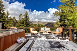 An outdoor deck with a hot tub, two cushioned chairs, and a table with a vase of flowers. - Lookout Drive 5 Bedrooms PLO-6599 by KBM (Park City)
