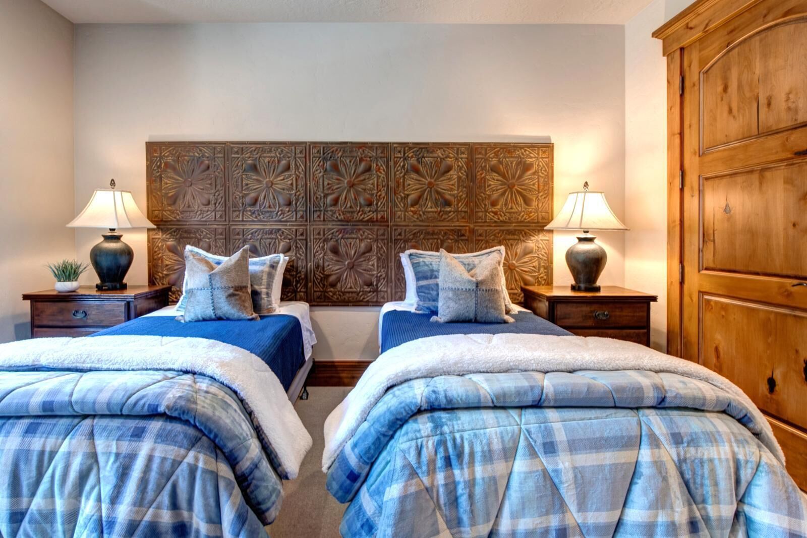Een slaapkamer met een tweepersoonsbed, een decoratieve hoofdbord, twee nachtkastjes met lampen en een houten garderobe.